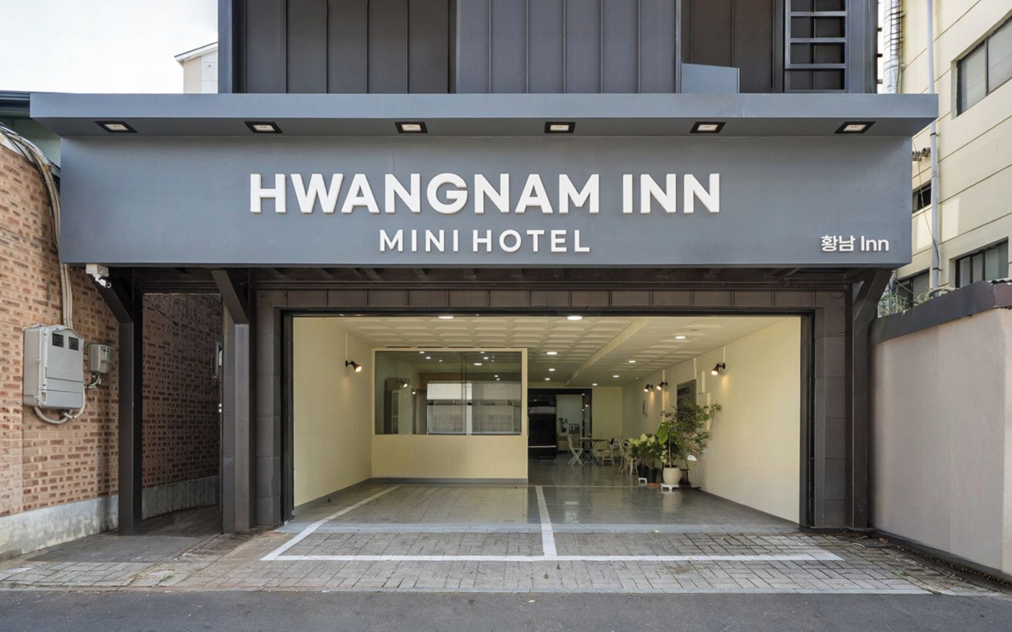 L’entrée de l’hôtel Hwangnam Inn Mini se distingue par une porte en verre transparent et une enseigne placée au-dessus.
