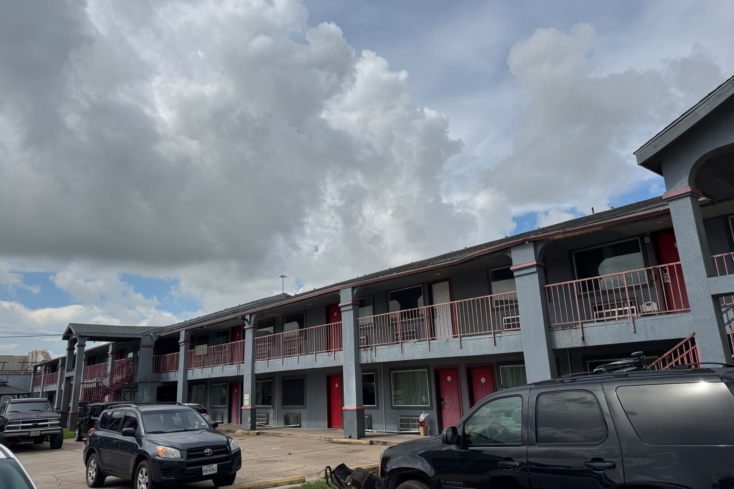 A multi-story building with balconies and a parking area.