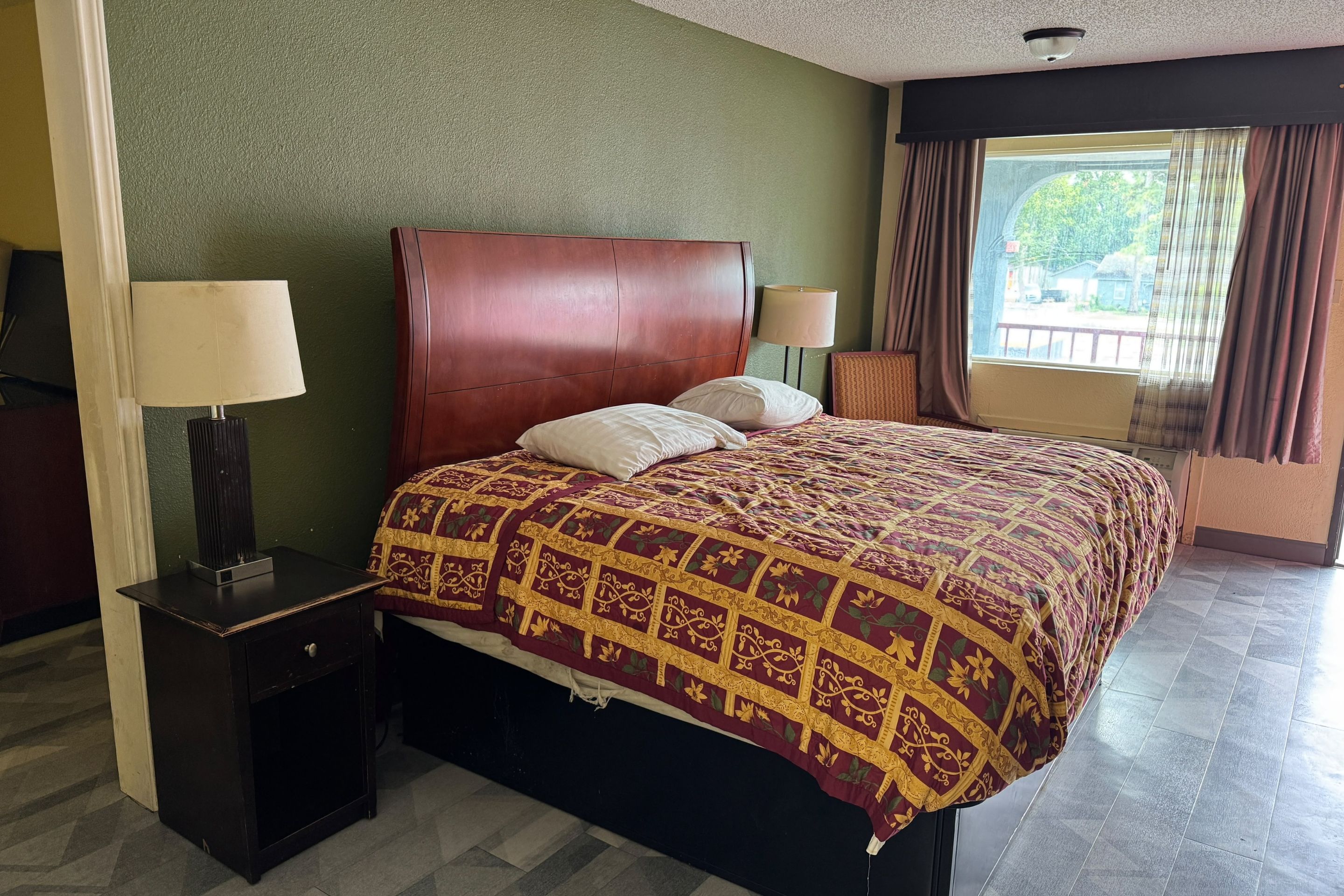 A hotel room with a large bed, two bedside lamps, a small table, and a view of the outdoors through a window.