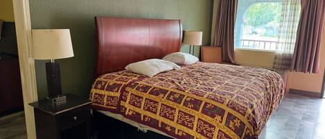 Quarto de hotel com uma cama grande, duas luminárias de cabeceira, uma mesinha e vista para o exterior pela janela.