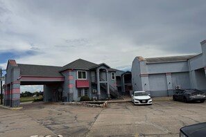 A building with a covered entrance, a staircase, and a parking area with two cars. - Blue Way Inn & Suites Houston - Katy/Rosenberg (Rosenberg)