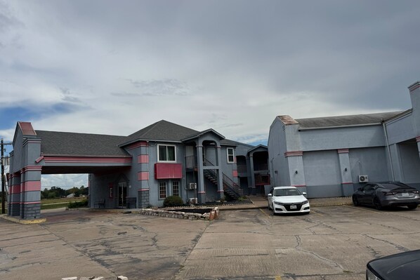 A building with a covered entrance, a staircase, and a parking area with two cars. - Blue Way Inn & Suites Houston - Katy/Rosenberg (Rosenberg)