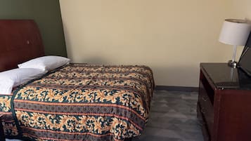 A single bed with a patterned bedspread, a bedside table with a lamp, and a dresser with a mirror.