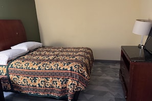 A single bed with a patterned bedspread, a bedside table with a lamp, and a dresser with a mirror. - Blue Way Inn & Suites Houston - Katy/Rosenberg (Rosenberg)