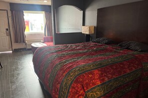 A hotel room with a large bed, a small round table, a window with curtains, and a wall-mounted lamp. - Blue Way Inn & Suites Houston - Katy/Rosenberg (Rosenberg)