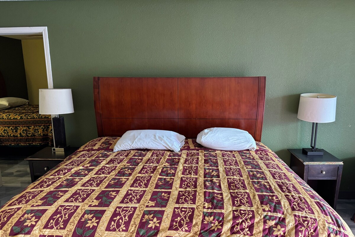 A hotel room with a large bed, two bedside lamps, a wooden headboard, and a green wall.