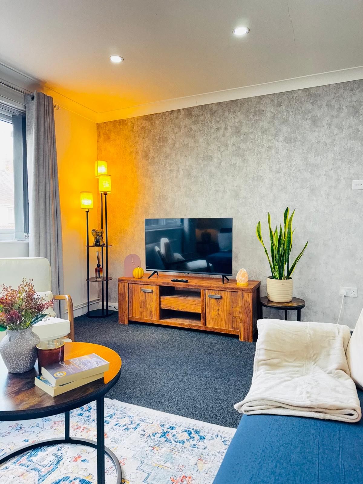 A modern living room with a flat-screen TV, wooden entertainment unit, a potted plant, and a cozy sofa.