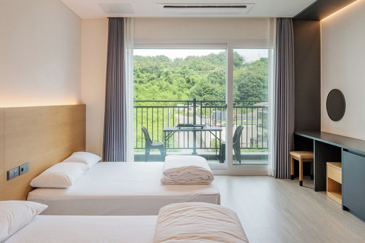 A hotel room with two beds, a desk, and a balcony with a table and chairs.