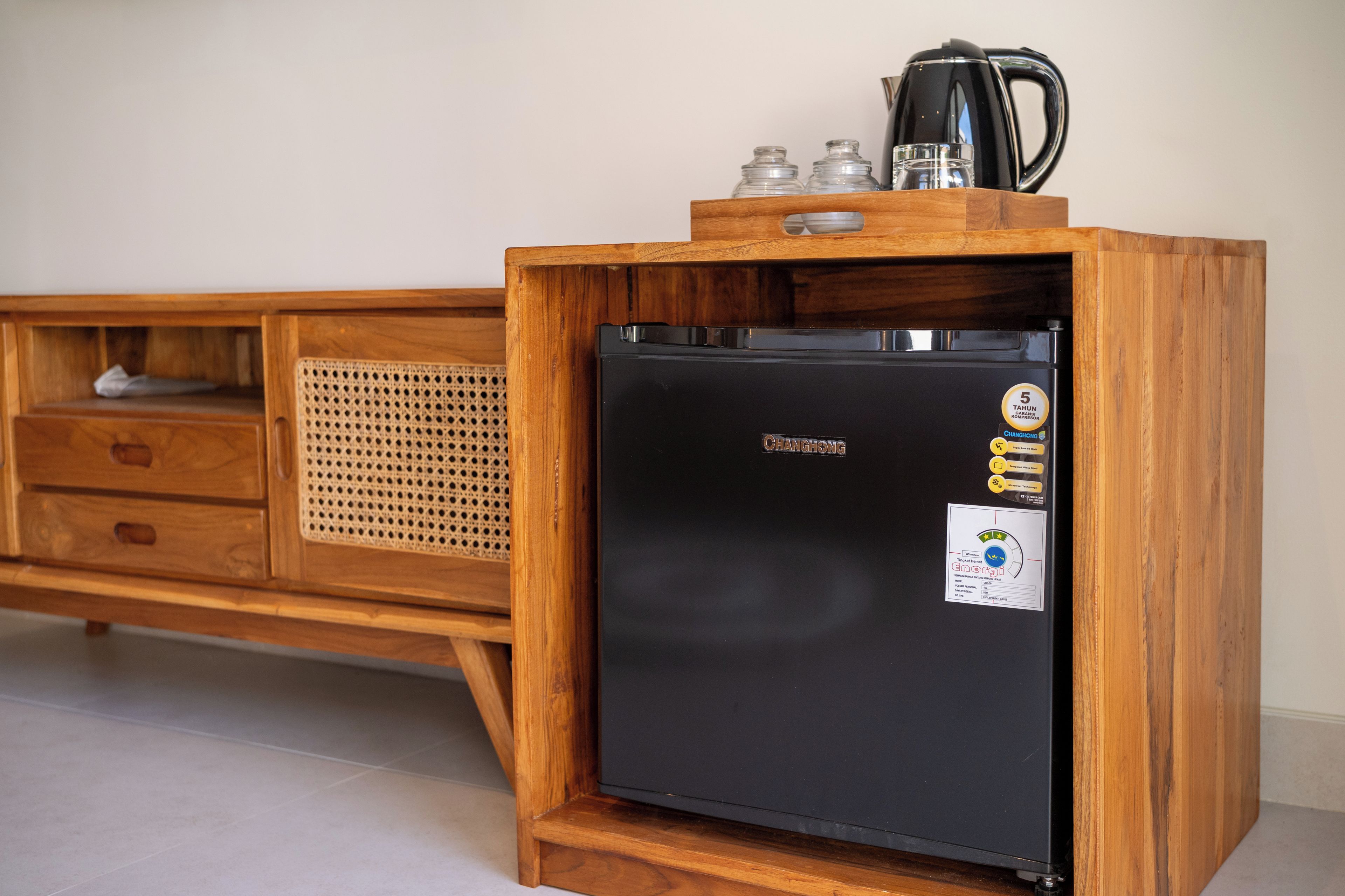 Un refrigerador negro compacto con gabinete de madera, una cesta tejida y una cafetera encima.