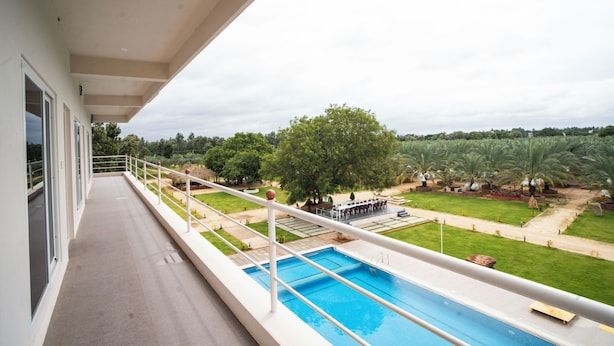 A balcony with a view of a swimming pool and a landscaped garden. - Habba Dates Village (CHIKKABALLAPURA)