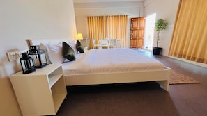 A hotel room with a bed, bedside table, lamp, and a view of the outside.
