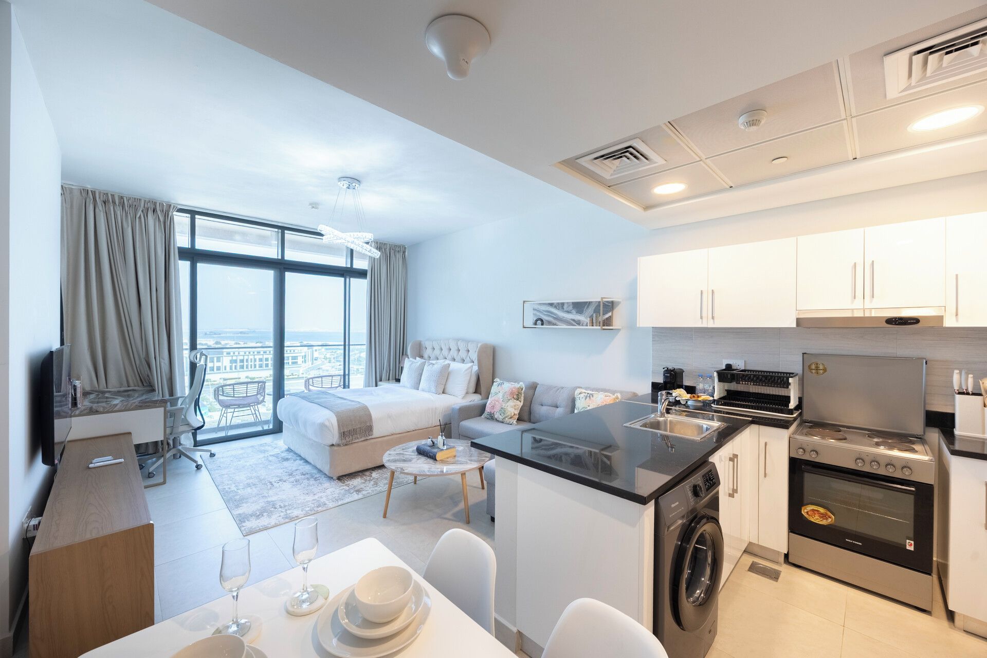 A modern hotel room with a balcony, a kitchenette, and a dining area.