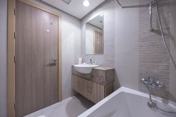 A modern bathroom with a wooden door, a sink with a marble countertop, a large mirror, and a walk-in shower.