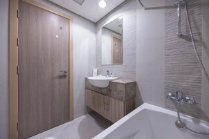 Un baño moderno con puerta de madera, un lavamanos con encimera de mármol, un espejo grande y una ducha a pie.