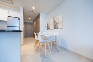 Una cocina moderna con un refrigerador empotrado, un comedor con una mesa y sillas blancas, y un pasillo que lleva a una puerta.