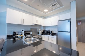A modern kitchen with white cabinets, a stainless steel refrigerator, a stove, and a sink. - Bloomfields Studio in Soho Square B (Abu Dhabi)
