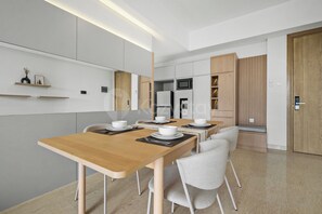 A modern dining area with a wooden table set for four, a microwave, and a refrigerator in the background. - Chiro by Kozystay - Tanjung Barat (Jakarta)