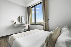 A hotel room with a bed, a desk with a chair, a round mirror, and a window with curtains. - Chiro by Kozystay - Tanjung Barat (Jakarta)