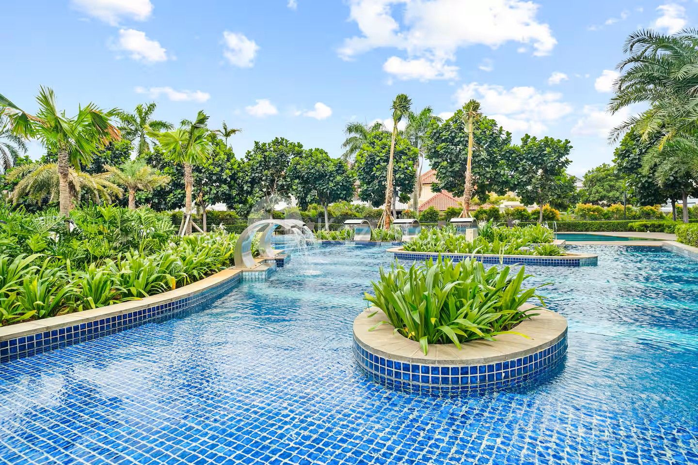 Piscina com piso azulejado, cercada por plantas tropicais e palmeiras.