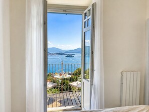 A room with a balcony overlooking a body of water and a distant mountain range. - Villa Anna Isole Borromee No. 11 (Stresa)