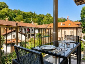 A terrace with a table set for dining, surrounded by a metal fence, overlooking a residential area with houses and greenery. - Villa Anna Isole Borromee No. 11 (Stresa)
