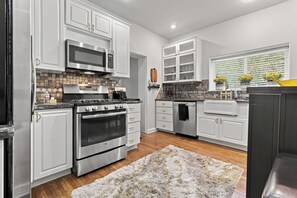 A modern kitchen with stainless steel appliances, white cabinetry, and a patterned backsplash. - Historic Bruce Goff Home with Pool, Hot tub & Sauna near Utica Square (Tulsa)