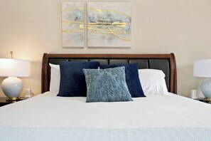 A neatly made bed with a white comforter and blue and white pillows, a wooden headboard, and two bedside lamps on either side. - Historic Bruce Goff Home with Pool, Hot tub & Sauna near Utica Square (Tulsa)