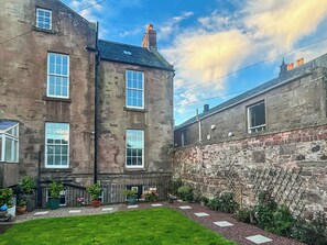 A courtyard with a stone wall, a grassy lawn, and potted plants. - 4 bedroom accommodation in Montrose (Montrose)