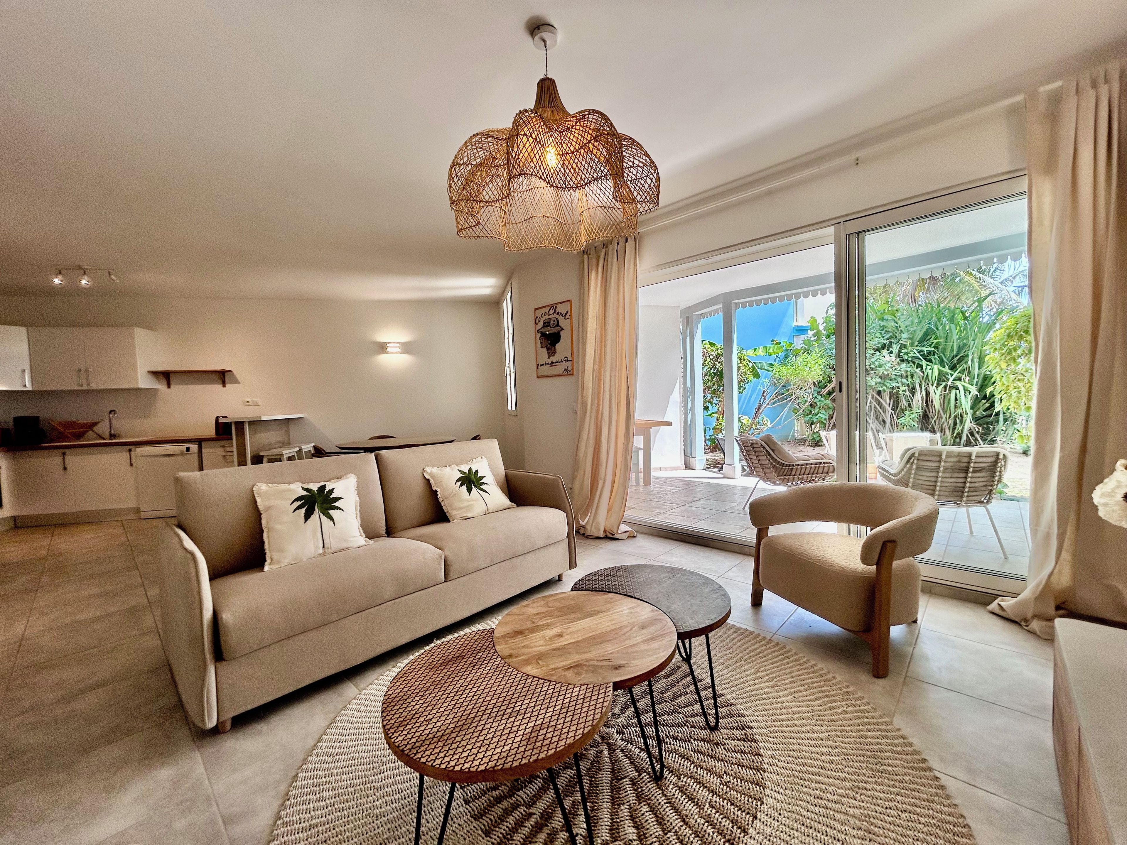 A modern living room with a sofa, two round tables, a hanging light fixture, and a view of the outdoors.
