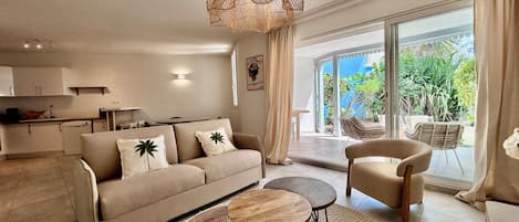 A modern living room with a sofa, two round tables, a hanging light fixture, and a view of the outdoors.