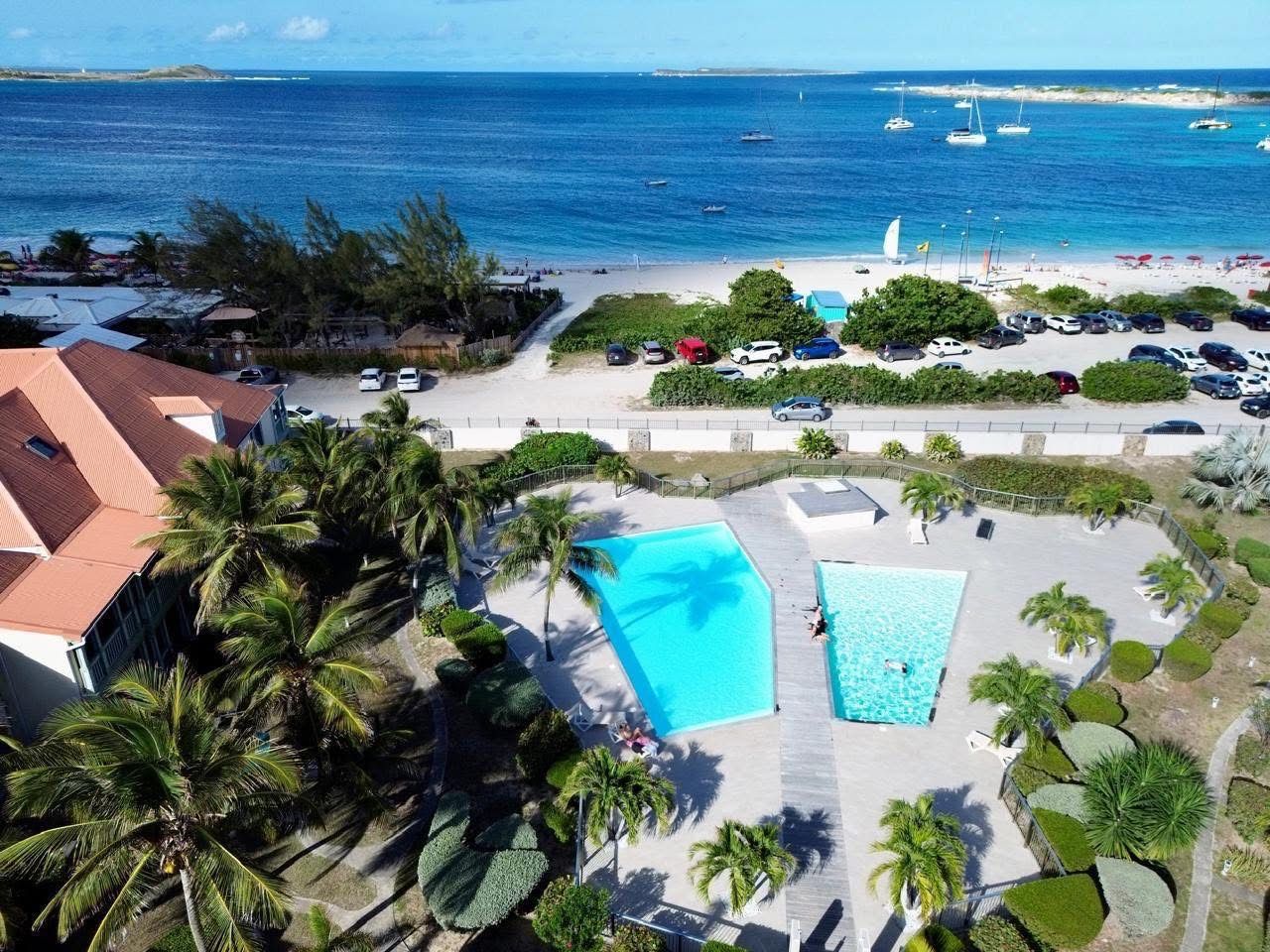 A resort with a large swimming pool, a beach area, and a view of the ocean.