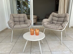 Two beige cushioned chairs with a white table between them, featuring two orange glass candle holders. - Elegant 2-Bedroom Apartment in the Heart of Orient Bay (Saint-Martin)