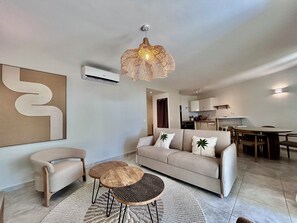 A modern living room with a sofa, a coffee table, and a dining area with a table and chairs. - Elegant 2-Bedroom Apartment in the Heart of Orient Bay (Saint-Martin)