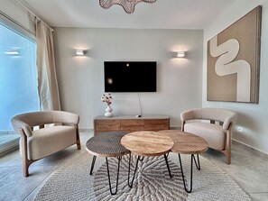 A modern living room with a flat-screen TV, two armchairs, a coffee table, and a decorative vase. - Elegant 2-Bedroom Apartment in the Heart of Orient Bay (Saint-Martin)