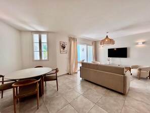 A modern living room with a sofa, TV, and dining area with chairs and a table. - Elegant 2-Bedroom Apartment in the Heart of Orient Bay (Saint-Martin)