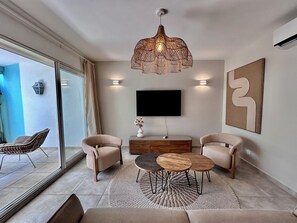 Ein modernes Wohnzimmer mit einem großen Fenster, einem Flachbildfernseher, einer Wanddekoration und einer außergewöhnlichen Pendelleuchte.