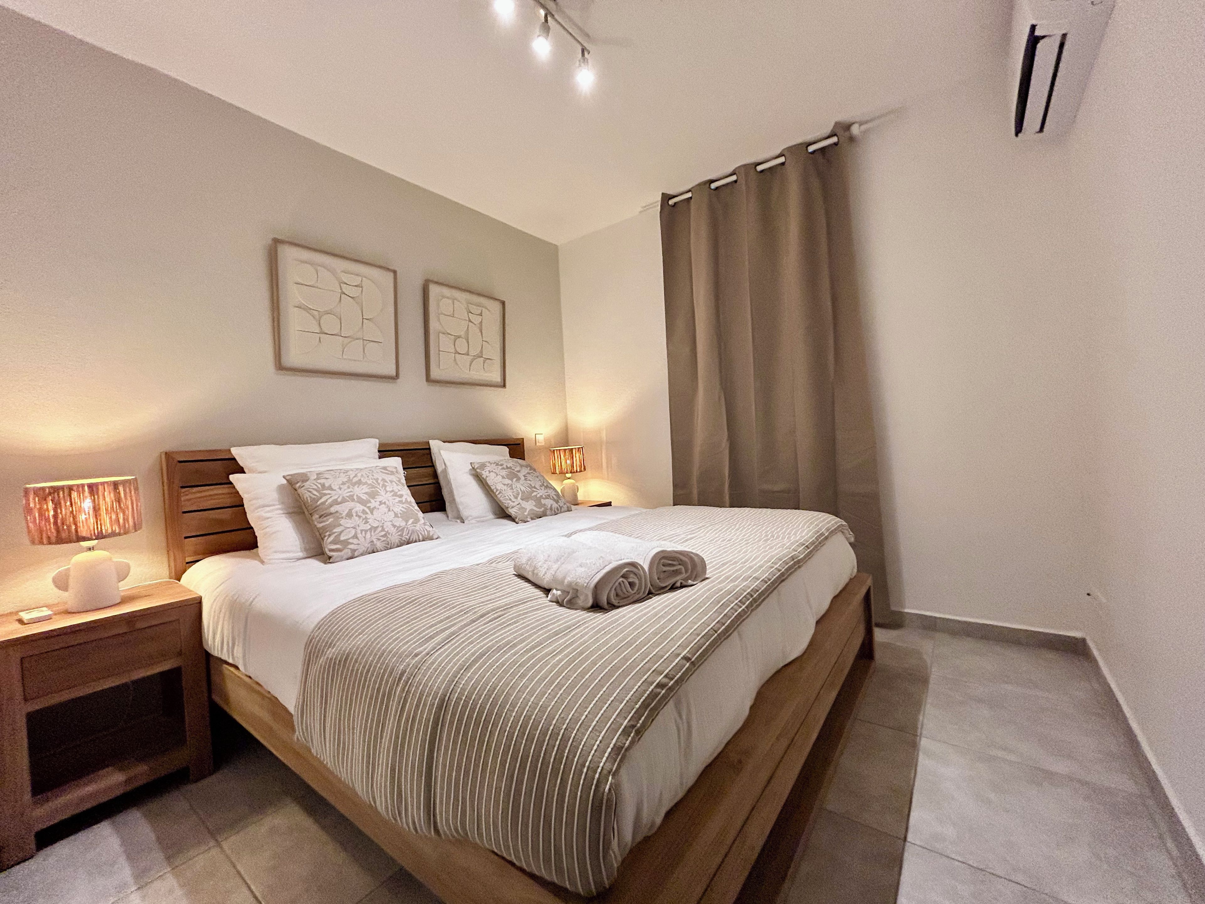 Ein ordentlich bezogenes Bett mit gestreifter Decke und Kissen, einer Nachttischlampe und einer Wand-Klimaanlage.