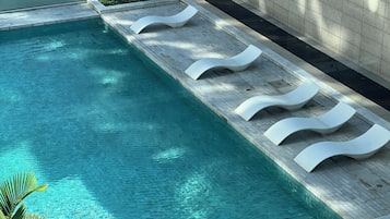 A swimming pool with clear water, surrounded by a tiled deck and white lounge chairs.