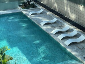 Una piscina con agua cristalina, rodeada por un solárium con baldosas y sillones blancos.