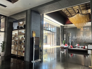 A modern lobby with a glass partition, a reception desk, and a seating area with a sofa and chairs.