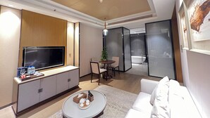 Una habitación de hotel moderna con televisor de pantalla plana, sofá, zona de comedor con mesa y sillas, y baño independiente con bañera.