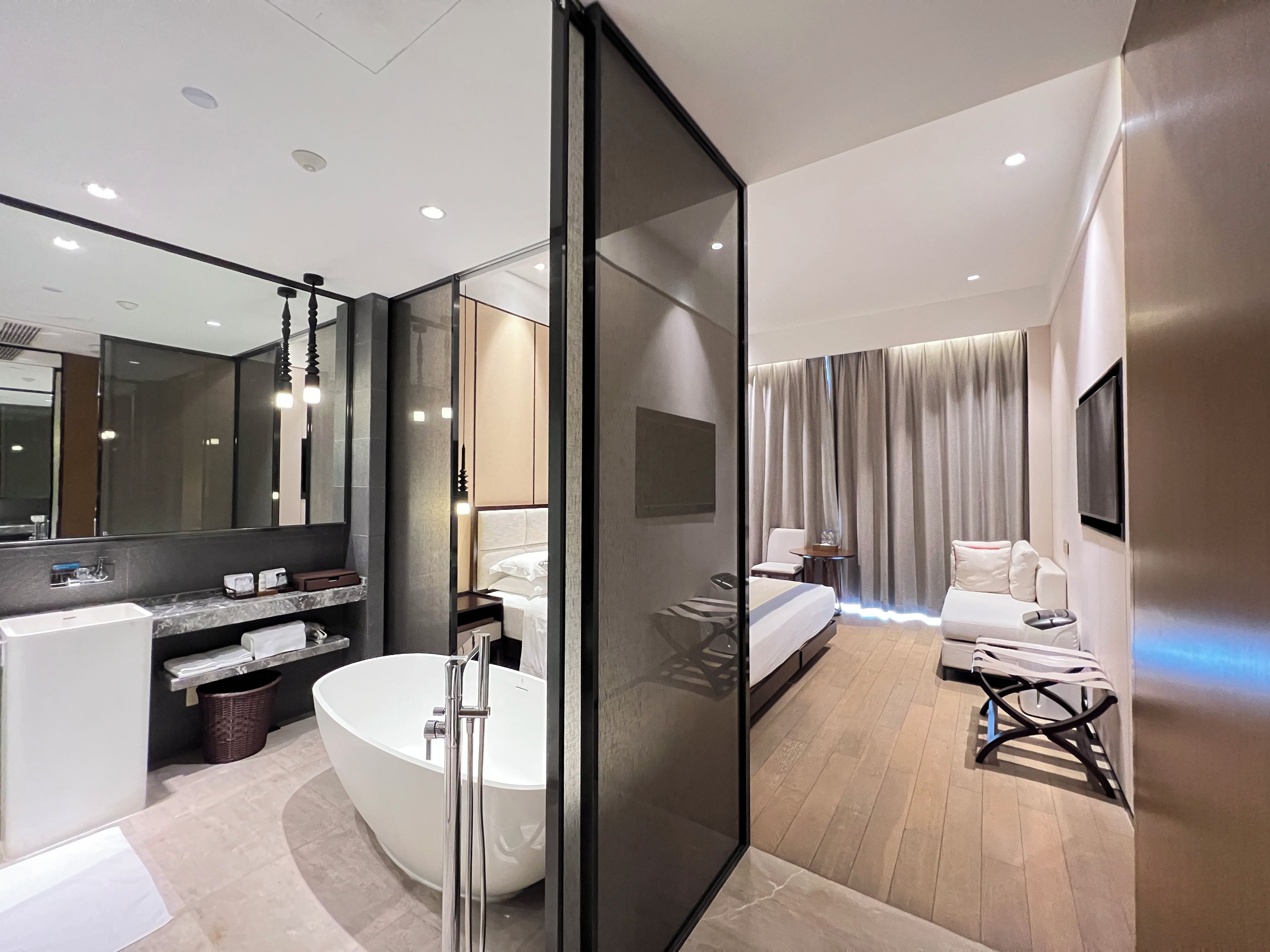 Un baño de hotel moderno con una bañera independiente, un espejo grande y un tocador con lavamanos y perchero para toallas.