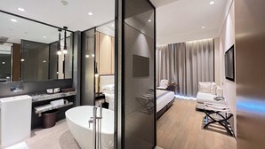 Un baño de hotel moderno con una bañera independiente, un espejo grande y un tocador con lavamanos y perchero para toallas.