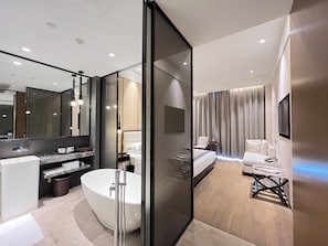 Un baño de hotel moderno con una bañera independiente, un espejo grande y un tocador con lavamanos y perchero para toallas.