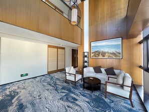 A modern hotel lobby with a large seating area, a painting of a coastal landscape, and a patterned carpet.