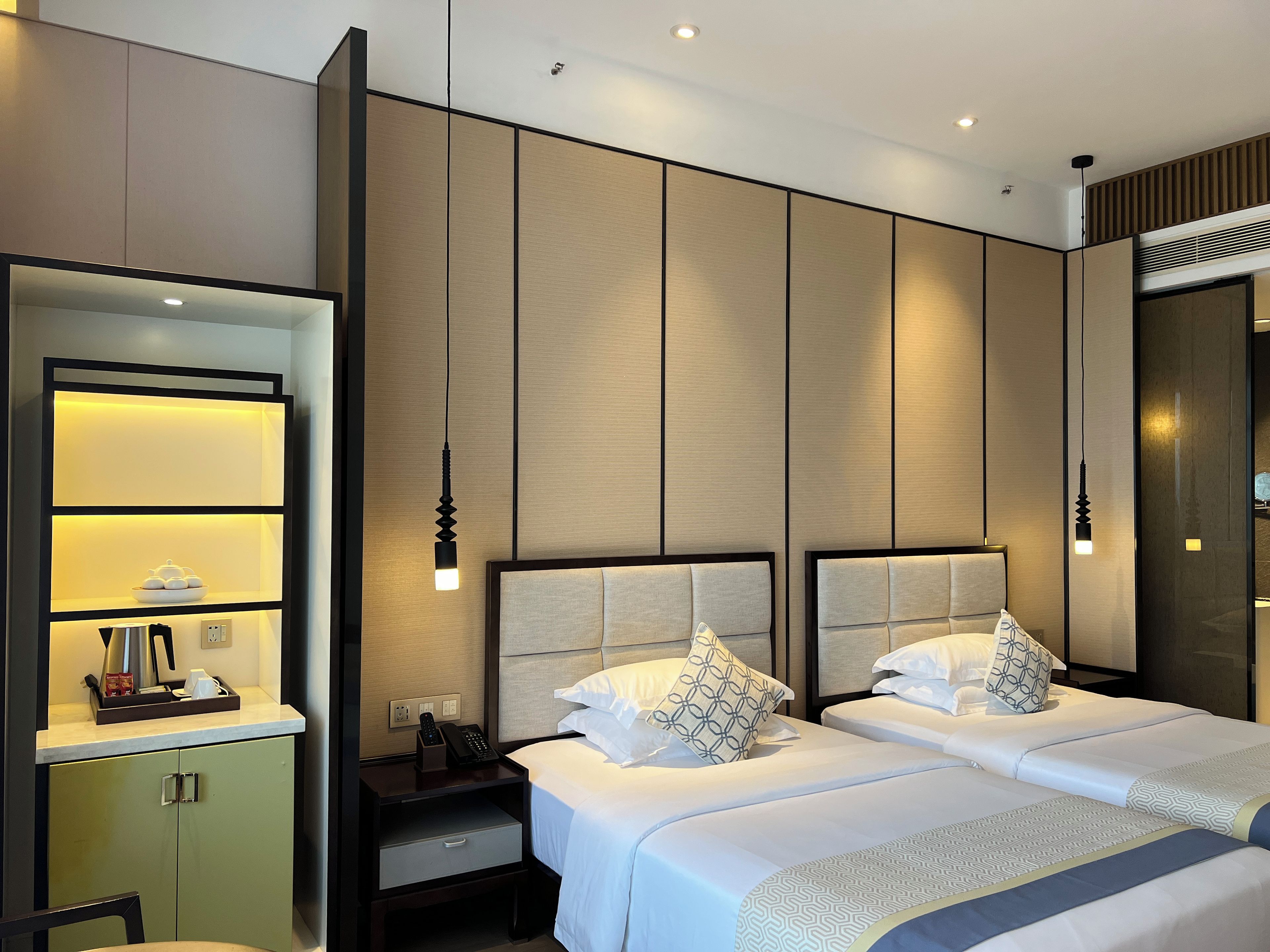 A hotel room with a bed, bedside tables, a nightstand, a mirror, and a wall-mounted shelf.