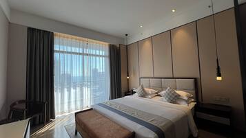 A modern hotel room with a large bed, a desk, and a view of the city.