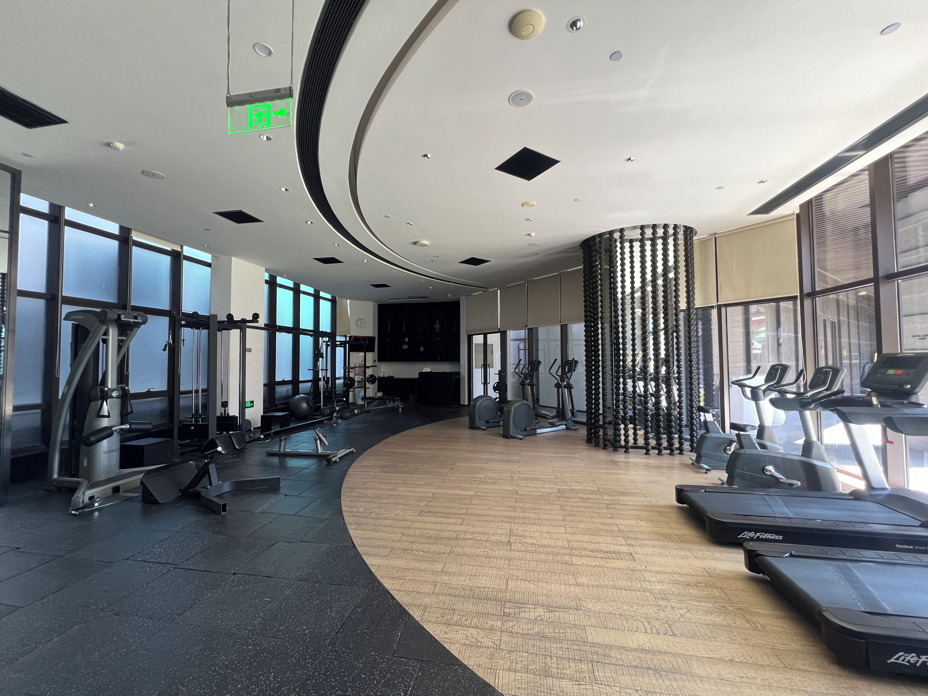 A gym with cardio equipment, weight machines, and a curved wooden floor.