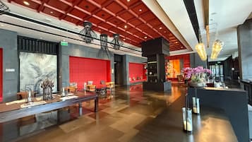 A modern hotel lobby with a red and black color scheme, a reception desk, and a seating area with tables and chairs.