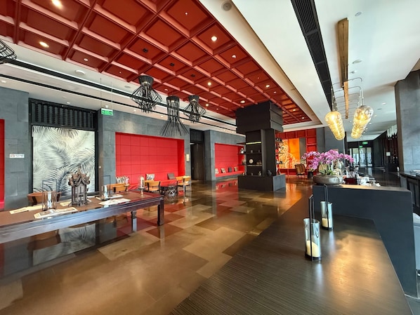 A modern hotel lobby with a red and black color scheme, a reception desk, and a seating area with tables and chairs.